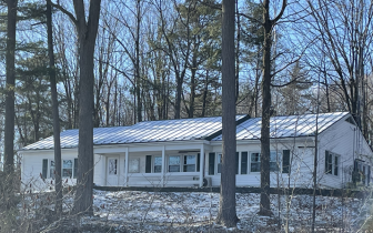 White single-story building, clapboard siding, just off highway behind trees